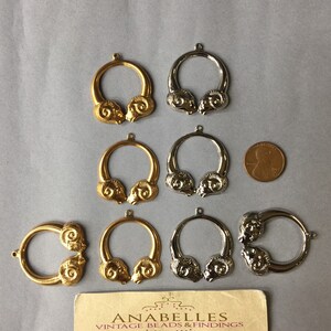 May include: A collection of gold and silver-toned metal ram head pendants. The pendants are circular with a ram head design on each side. A business card and a penny are also in the image.