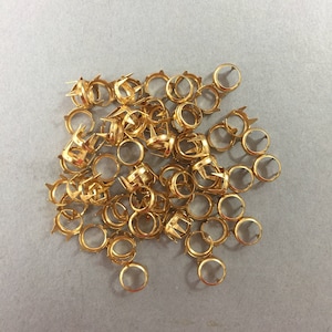 Può includere: Un mucchio di impostazioni in metallo dorato per chiodi decorativi. Le impostazioni sono rotonde con un centro appuntito.