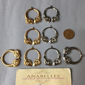May include: A collection of gold and silver-colored ram head pendants, some with a circular design. A penny is included for size reference. A business card for Anabelles Vintage Beads & Findings is also present.