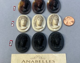 May include: Nine vintage cameo buttons with different designs. Three are brown, three are white, and three are black. The buttons are oval shaped and feature a woman's face in relief. The buttons are arranged in three rows of three. The image also includes a business card for Anabelles Vintage Beads & Findings.