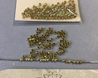 May include: A close-up of a bag of gold-colored beads, with some beads scattered on a white surface. The bag is labeled "Anabelles Vintage Beads & Finding".