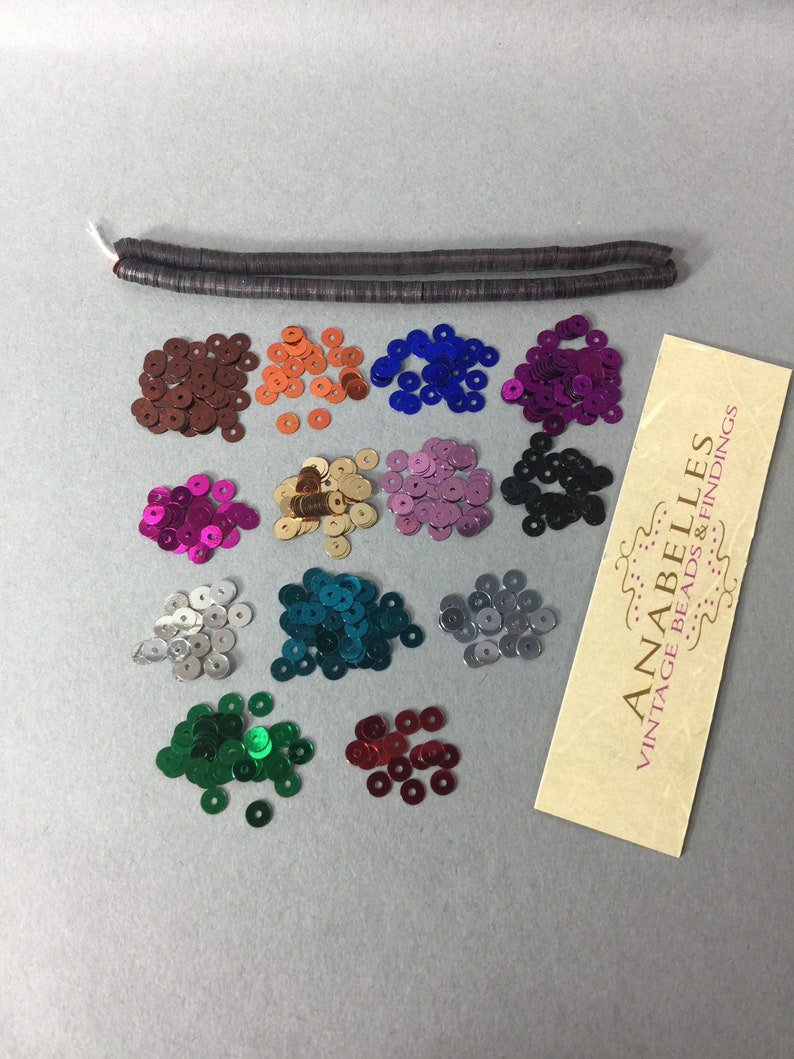 May include: Assortment of 12 colors of round sequins, each pile containing approximately 50 sequins.  The sequins are arranged in rows of three.  A brown, flat, beaded cord is included.  The image also includes a business card for Anabelles Vintage Beads & Findings.