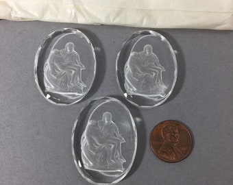 May include: Three clear glass oval-shaped pendants with a raised image of Michelangelo's Pieta sculpture. The pendants are approximately the size of a US penny.