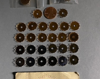 以下が含まれることがあります： 装飾的な銀色のフィリグリーデザインが施された、金色の丸いビーズキャップが25個集められています。ビーズキャップは白い表面に並べて配置されています。画像には、Anabelles Vintage Beads & Findingsのビジネスカードも含まれています。