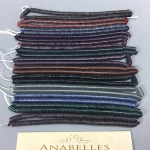 May include: A collection of 18 strands of iridescent, flat, round, plastic beads in various colors, including black, brown, purple, green, and gray. The beads are arranged in rows and are all the same size. The beads are labeled "Anabelles Vintage Beads & Findings".
