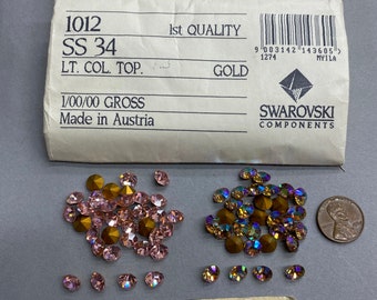 Può includere: Primo piano di due sacchetti di perline di vetro color rosa chiaro. I sacchetti sono etichettati con "1012 SS 34" e "1a qualità Oro". Le perline sono realizzate da Swarovski e sono 1/00/00 lordo. I sacchetti sono su una superficie bianca.