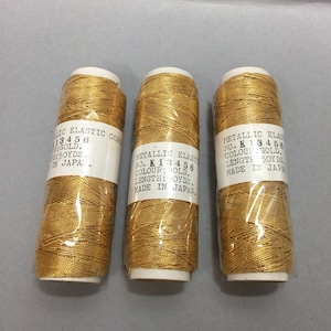 May include: Three spools of gold metallic elastic cord, each labeled "Metallic Elastic No. K 13456, Colour: Gold, Length: 50 yds, Made in Japan."