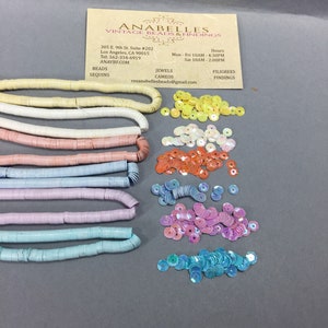 May include: Assortment of pastel colored plastic sequins and beads. The beads are in rows of different colors, including white, pink, lavender, light blue, and turquoise. The sequins are in piles of yellow, iridescent, orange, pink, and turquoise.