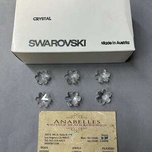 May include: A box of clear crystal snowflake beads from Swarovski. The box is white with black text that reads "ART. 6707", "25 MM", "2/12 GROSS", "SPECIAL", "CRYSTAL", "SWAROVSKI", and "Made in Austria".