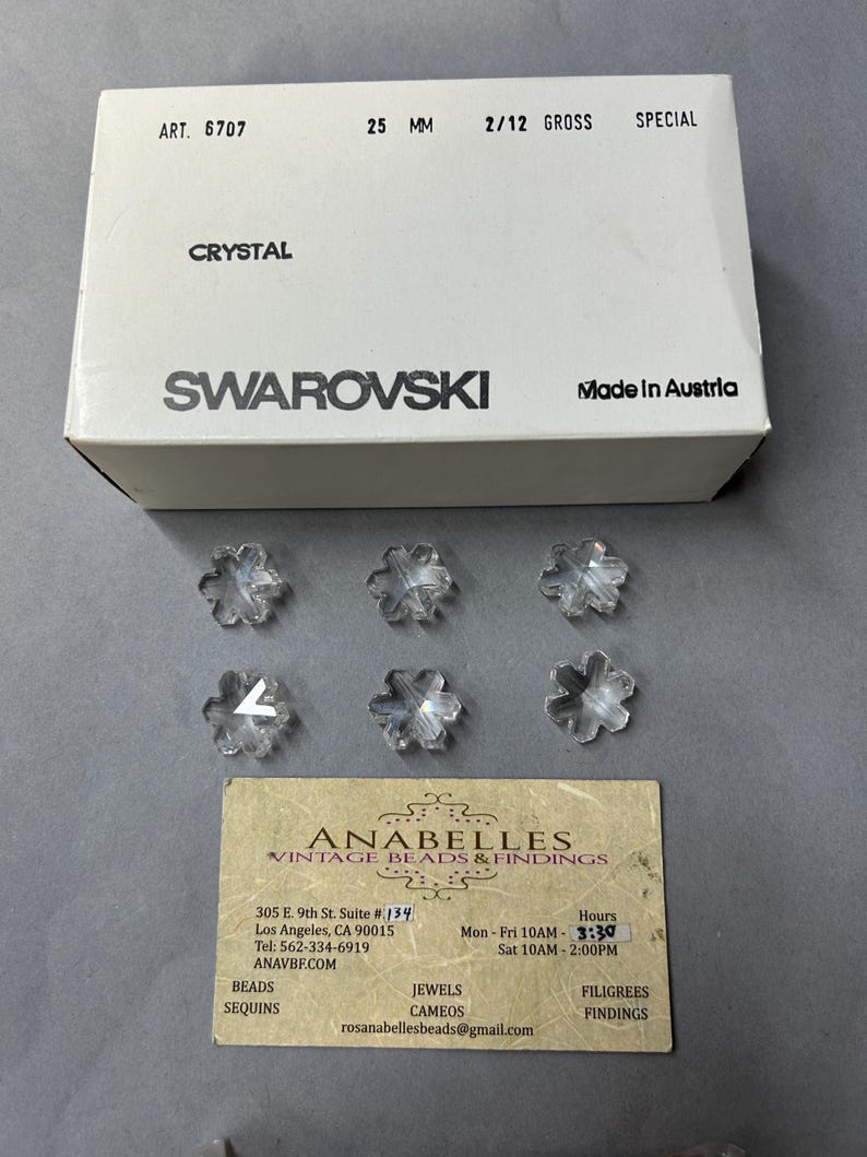 May include: A box of clear crystal snowflake beads from Swarovski. The box is white with black text that reads "ART. 6707", "25 MM", "2/12 GROSS", "SPECIAL", "CRYSTAL", "SWAROVSKI", and "Made in Austria".