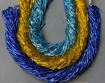 May include: Three strands of glass beads in blue, light blue, and gold. The beads are small and cylindrical, and they are arranged in a circle. The beads are for jewelry making.