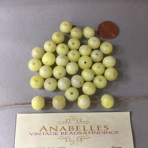 Op de afbeelding: Een stapel van 25 gele en witte glazen kralen met een witte draad erdoorheen. De kralen zijn rond en hebben een swirl-patroon. Een visitekaartje voor Anabelles Vintage Beads & Findings bevindt zich in de rechterbenedenhoek van de afbeelding.