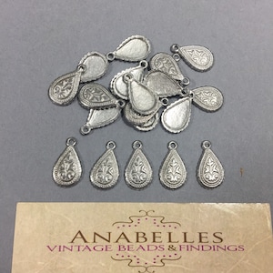 May include: A group of 15 silver teardrop-shaped metal charms with a decorative floral design. The charms have a loop at the top for attaching to jewelry or other crafts.