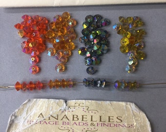 May include: Assortment of iridescent glass beads in orange, yellow, and blue colors. The beads are arranged in three groups and a string of beads is shown in the bottom of the image. The image also includes a business card for Anabelles Vintage Beads & Findings.