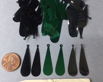 Puede incluir: Un montón de lentejuelas de color negro y verde en forma de lágrima con un agujero en la parte superior. Las lentejuelas están dispuestas en dos montones, uno de negro y otro de verde. Hay una moneda de un centavo en la esquina inferior izquierda de la imagen. La imagen también incluye una tarjeta de visita para Anabelles Vintage Beads & Findings, con la dirección 305 E. 9th St. Suite #134 y el horario de atención: Lun-Vie 10:00-16:30.
