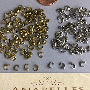 May include: A close-up of two piles of metal clasps. One pile is gold and the other is silver. The clasps are small and have a simple design. There are also a few clasps scattered around the piles.