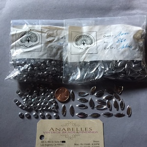 Op de afbeelding: Een afbeelding van vintage kralen en bevindingen, waaronder twee verzegelde zakken met zilverkleurige kralen, losse kralen en een visitekaartje. Op het visitekaartje staat "ANABELLES VINTAGE BEADS & FINDINGS".