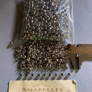 May include: A bag of silver metal rivets, with a few scattered on a white surface. A ruler is in the background. The image includes a business card for Anabelles Vintage Beads & Findings, with the address 305 E. 9th St. Suite #134 Los Angeles, CA 90015, Tel: 562-334-6919, and opening hours.