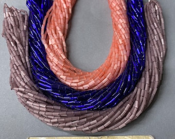 May include: Three strands of glass beads in different colors. The strands are pink, blue, and purple. The beads are all the same size and shape, and they are arranged in a loose pile. The beads are for sale at a store called "Anabelles Vintage Beads & Findings".