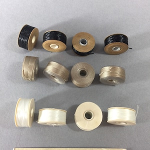 May include: A collection of 10 spools of thread in black, beige, and white. The spools are labeled "Anabelles Vintage Beads & Findings".