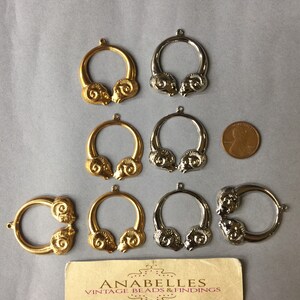 May include: A collection of vintage metal ram head charms in gold and silver tones. The charms are circular with a ram head design on each side. A penny is included for size reference. A business card is also present.
