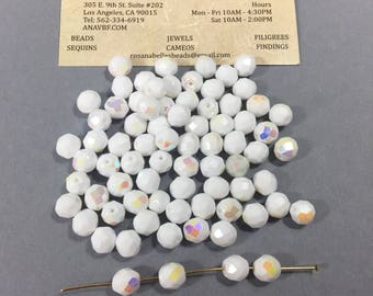 May include: A pile of white iridescent glass beads with a few beads strung on a gold wire. The beads are faceted and have a rainbow sheen.