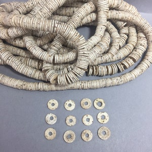 May include: A large pile of off-white, round, flat, and speckled beads. A smaller group of the same beads are arranged in a grid pattern below the pile.