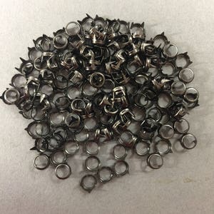 May include: A pile of silver metal eyelets with a pointed edge. The eyelets are arranged in a random pattern.