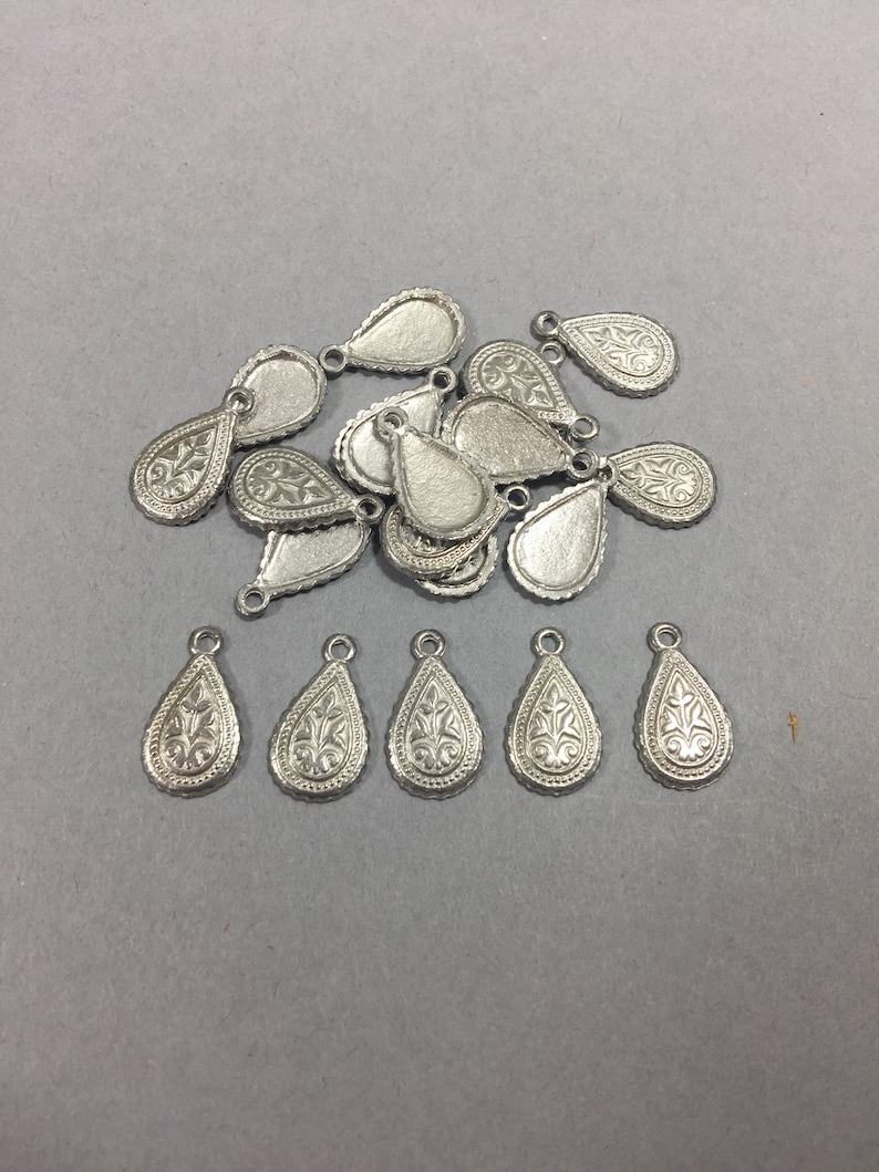 May include: A pile of silver teardrop-shaped charms with intricate floral designs. The charms have a loop at the top for attaching to jewelry or other crafts.