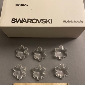 May include: Six clear crystal snowflake charms in a box labeled "Swarovski Crystal 25 mm 2/12 Gross Special Art. 6707 Made in Austria".