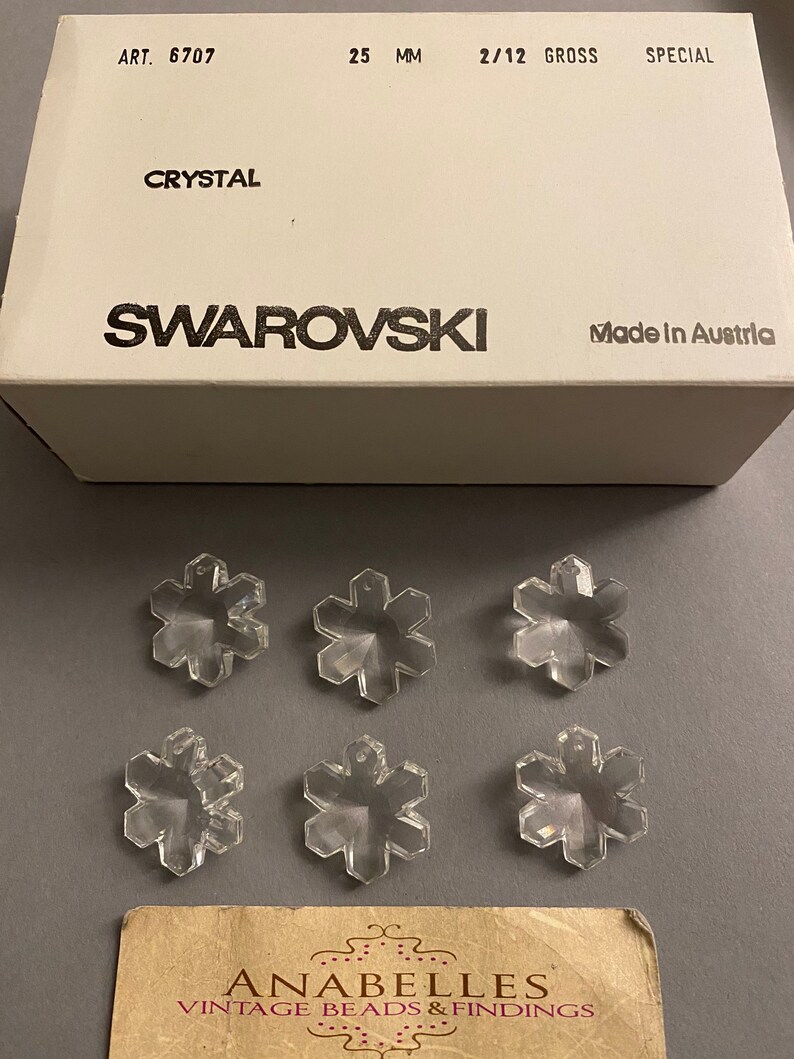 May include: Six clear crystal snowflake charms in a box labeled "Swarovski Crystal 25 mm 2/12 Gross Special Art. 6707 Made in Austria".