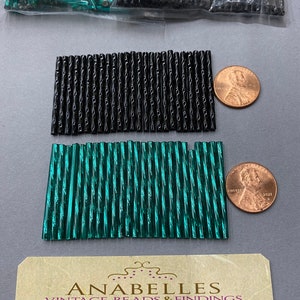 May include: Two bags of glass beads, one bag is black and the other is green. The beads are long and thin with a ribbed texture. The bags are sitting on a gray surface with a business card that says "Anabelles Vintage Beads & Findings" and "305 E. 9th St. Suite # 134 Los Angeles, CA 90015".