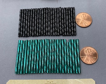 May include: Two bags of glass beads, one bag is black and the other is green. The beads are long and thin with a ribbed texture. The bags are sitting on a gray surface with a business card that says "Anabelles Vintage Beads & Findings" and "305 E. 9th St. Suite # 134 Los Angeles, CA 90015".
