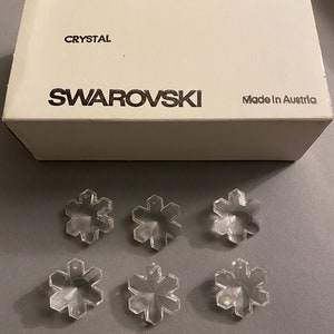 May include: A box of clear crystal snowflake charms, labeled "Swarovski" and "Made in Austria". The box also includes the text "ART. 6707", "25 MM", "2/12 GROSS", and "SPECIAL".