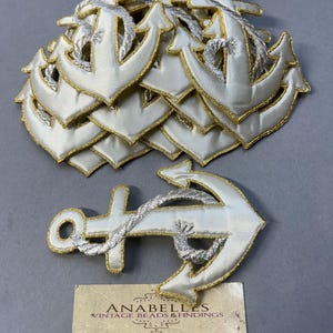 May include: A stack of white fabric anchor patches with gold and silver embroidery. The anchors have a rope detail. The patches are for sale at Anabelles Vintage Beads & Findings.