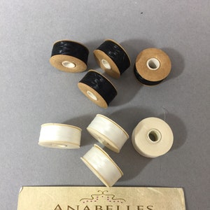 May include: Six spools of thread, three black and three white, on a business card for Anabelles Vintage Beads & Findings. The card lists the address 305 E. 9th St. Suite #202, Los Angeles, CA 90015 and the hours.