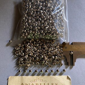May include: A bag of silver metal rivets, with a ruler measuring the size of the rivets. The rivets are approximately 1.2 cm in diameter. The bag is labelled "Anabelles Vintage Beads & Findings" with the address "305 E. 9th St. Suite #134 Los Angeles, CA 90015" and the hours "Mon - Fri 10AM - 3:30PM".