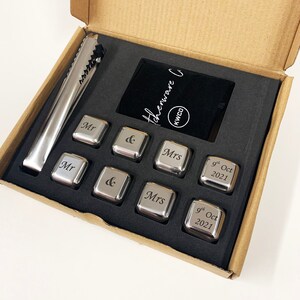 May include: A set of six stainless steel ice cubes in a brown box with a black velvet pouch. The ice cubes are engraved with the words "Mr", "&", "Mrs", and "9th Oct 2021".