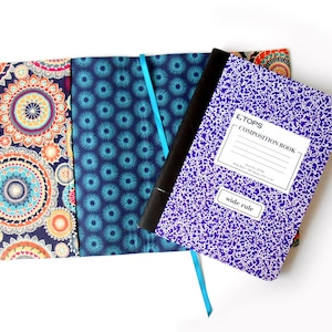 May include: A purple composition book with the text "Tops Composition Book" and "Wide Rule" on the cover. The book is wrapped in a fabric cover with a blue and white pattern and a colorful mandala pattern.