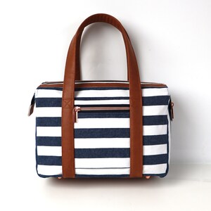 May include: A striped navy blue and white tote bag with brown leather handles and a zipper closure.