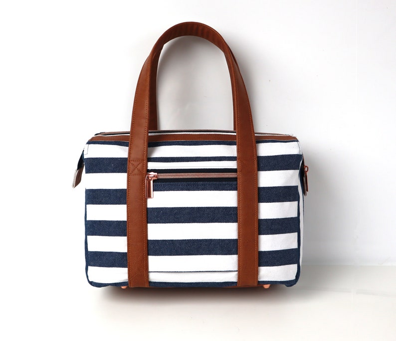 May include: A striped navy blue and white tote bag with brown leather handles and a zipper closure.