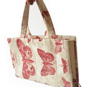 May include: A cream-colored fabric tote bag with red butterfly print and a key charm. The bag has two fabric handles.