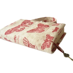 May include: A beige book cover with a red butterfly design. The cover has a red ribbon bookmark with a gold key charm.