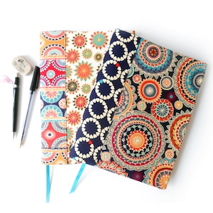 May include: Three fabric-covered notebooks with colorful mandala designs. The notebooks have blue, red, and white patterns.