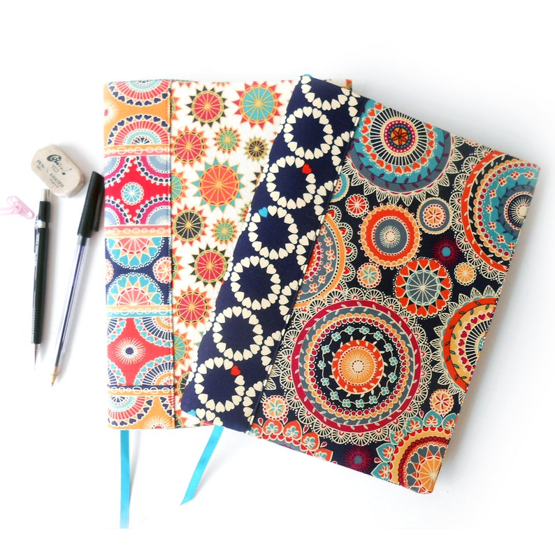May include: Three fabric-covered notebooks with colorful mandala designs. The notebooks have blue, red, and white patterns.
