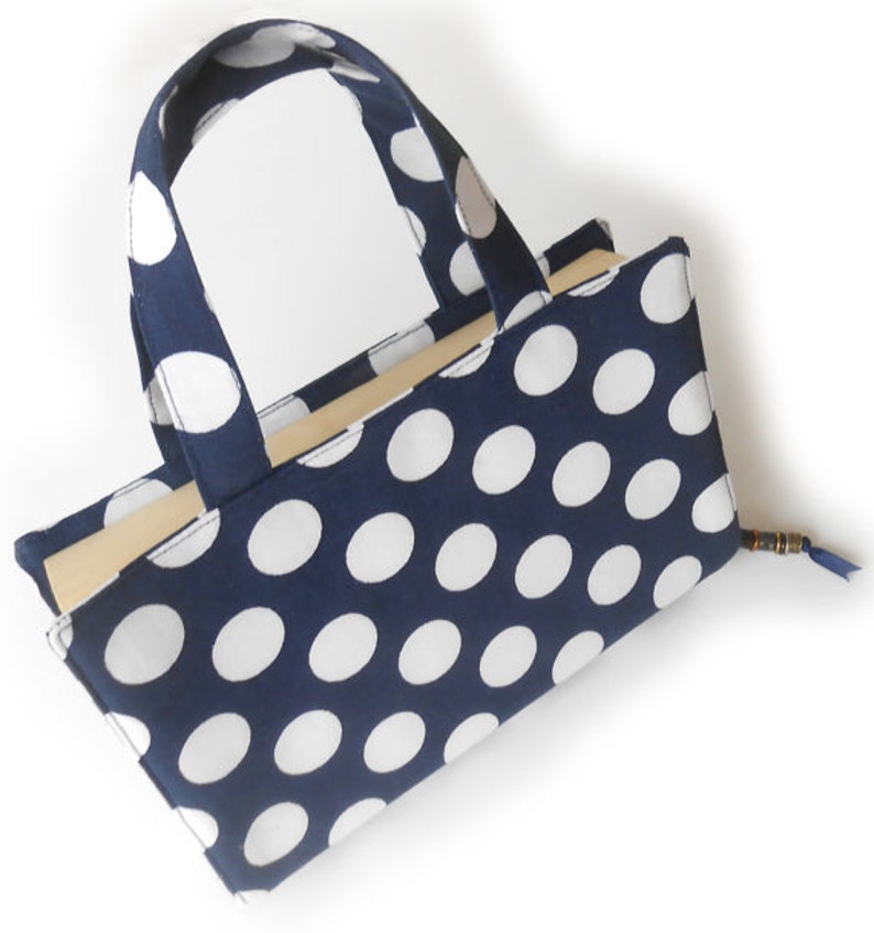 May include: A blue and white polka dot fabric tote bag with a handle. The bag is empty and has a light brown lining.