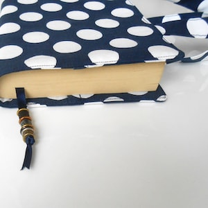 May include: A navy blue book cover with white polka dots. The cover has a matching strap and a blue ribbon bookmark with metal beads.