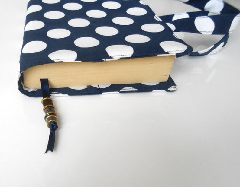 May include: A navy blue book cover with white polka dots. The cover has a matching strap and a blue ribbon bookmark with metal beads.