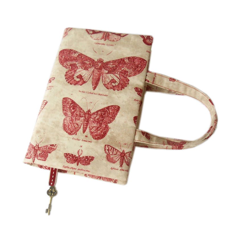 May include: A beige book bag with a red butterfly design. The bag has a fabric handle and a red bookmark with a key charm.