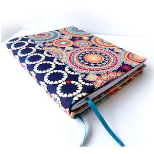 May include: A navy blue notebook with a colorful mandala pattern cover. The cover has a white and navy blue geometric pattern on the bottom half. The notebook has a teal ribbon bookmark.
